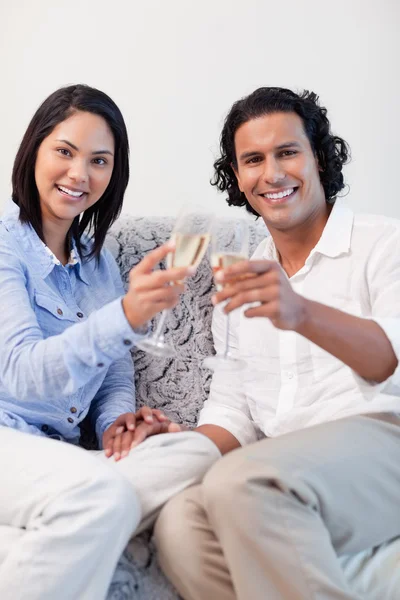 Счастливая пара пьет игристое вино на диване — стоковое фото