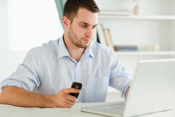 Empresario escribiendo en su portátil mientras sostiene el teléfono celular Imagen de archivo