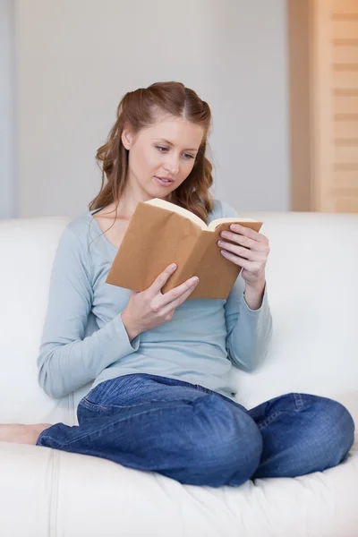Женщина на диване сосредоточилась на своей книге — стоковое фото