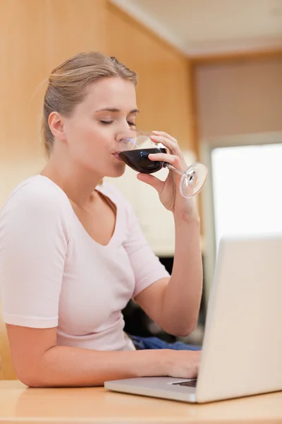 Ritratto di una giovane donna che usa un computer portatile mentre beve vino rosso — Foto Stock