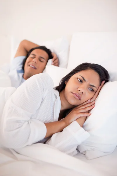 Displeased woman lying next to snoring boyfriend Stock Photo