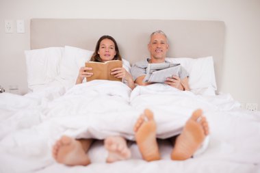 Man reading a newspaper while his wife is reading a book clipart