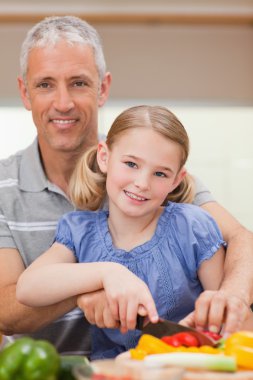 Portrait of a man slicing pepper with his daughter clipart