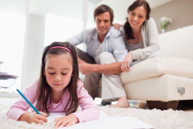 Little girl drawing with her parents in the background clipart