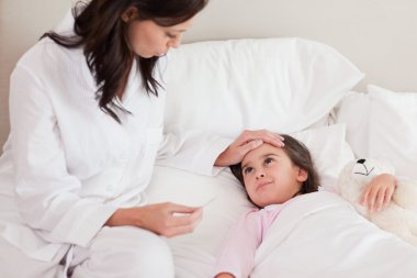 Mother checking on her daughter's temperature clipart