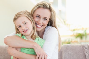 Mother hugging her daughter on sofa clipart