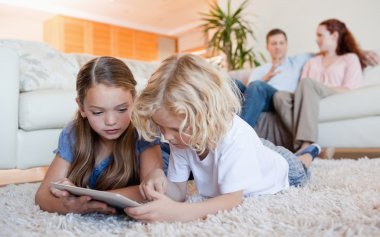 Siblings using tablet on the living room floor clipart