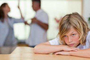 Worried looking boy with fighting parents behind him clipart