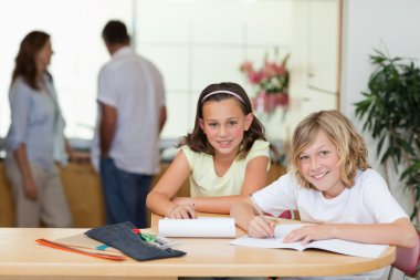 Siblings doing homework with their parents behind them clipart