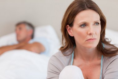 Sad woman on bed with her husband in the background clipart