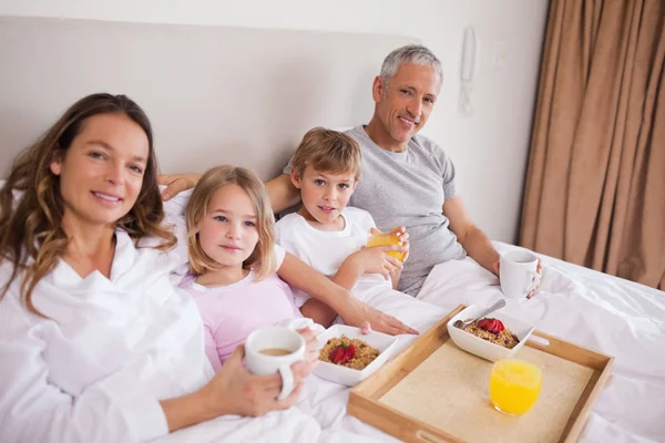 Улыбающаяся семья завтракает в спальне — стоковое фото