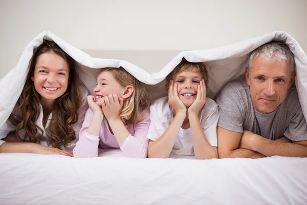 Glückliche Familie liegt unter einer Bettdecke — Stockfoto