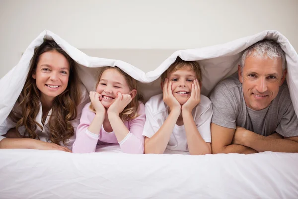 Verspielte Familie liegt unter einer Bettdecke — Stockfoto