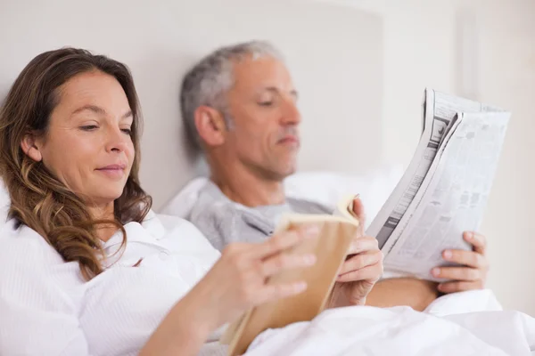 Woman reading a book while her husband is reading the news — Stock Photo, Image