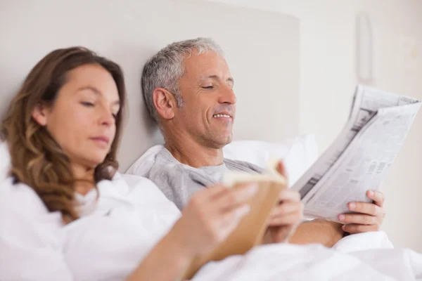 快乐的女人读一本书，而她的丈夫正在读取 newspa — 图库照片