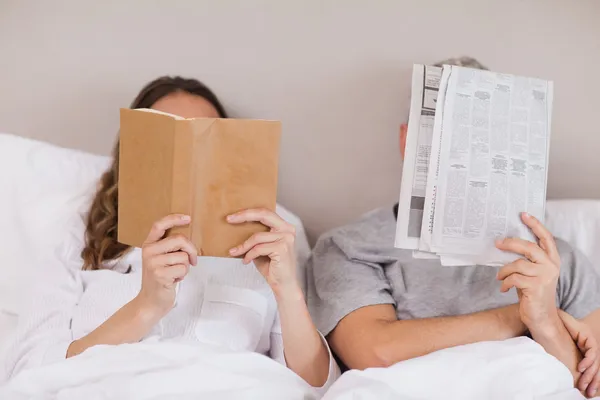 Mulher lendo um livro enquanto seu companheiro está lendo um jornal — Fotografia de Stock