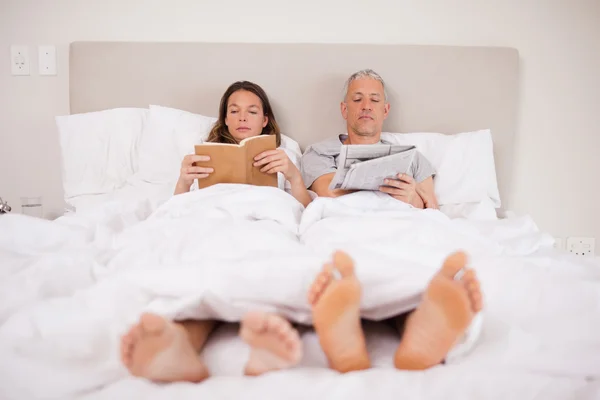 남자가 그의 아내는 책을 읽는 동안 뉴스를 읽고 — 스톡 사진