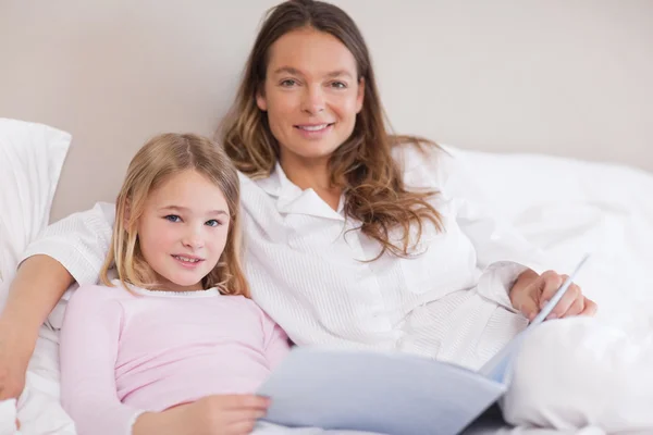 Leende tjej läser en bok med hennes mor — Stockfoto