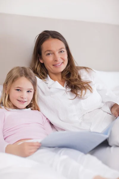 Portret dziewczynki uśmiechający się czytając książkę z matką — Zdjęcie stockowe
