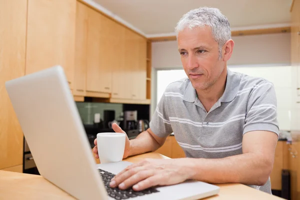 Kahve yudumlarken bir dizüstü bilgisayar kullanan adam — Stok fotoğraf
