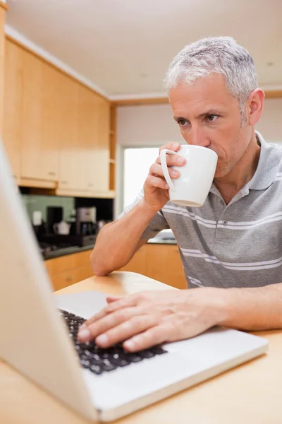 Retrato de um homem usando um laptop enquanto bebe café — Fotografia de Stock