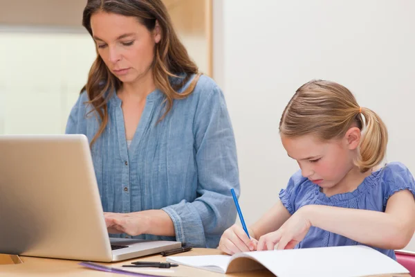 Kız annesi laptop kullanırken ödevini yapıyor — Stok fotoğraf