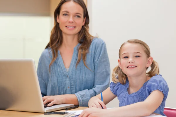 Dívka dělá její domácí úkoly, zatímco její matka používá notebook — Stock fotografie
