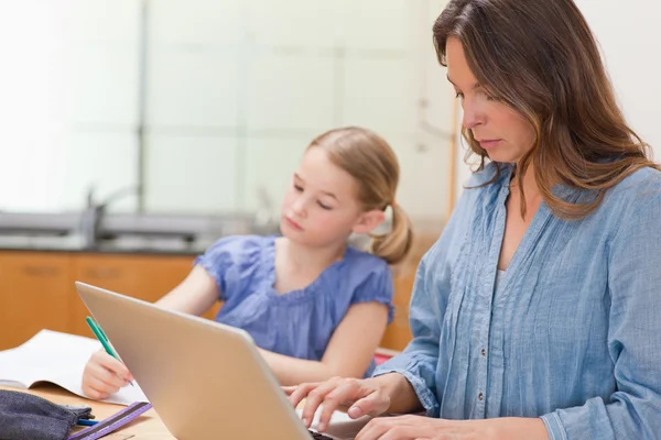 Klein meisje haar huiswerk terwijl haar moeder is met behulp van noteboo — Stockfoto