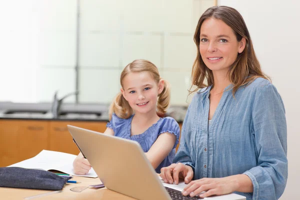 Chica haciendo su tarea mientras su madre está trabajando con el ordenador portátil — Foto de Stock