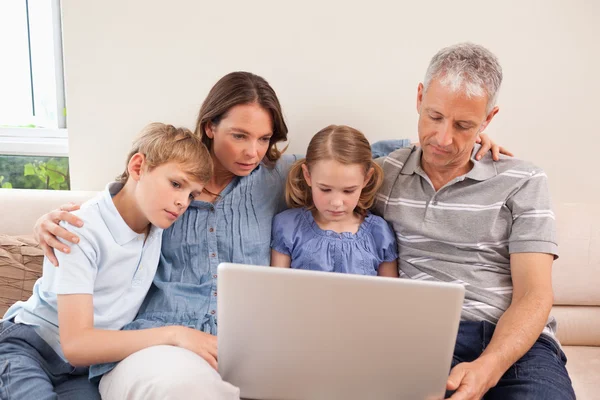 Família sentada em um sofá usando um laptop — Fotografia de Stock