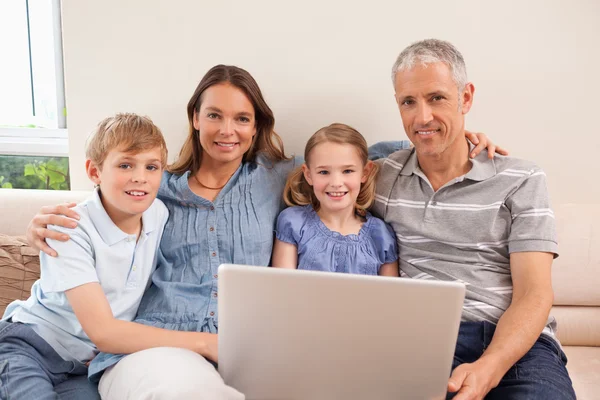 Aile bir dizüstü bilgisayar kullanarak bir koltukta oturan gülümsüyor — Stok fotoğraf