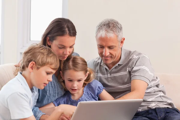 Szczęśliwa rodzina siedzi na kanapie przy pomocy pewien laptop — Zdjęcie stockowe