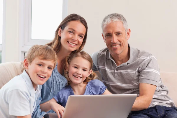 坐在沙发上使用的便携式计算机上的幸福家庭 — 图库照片