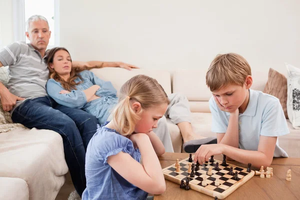 Братья и сёстры играют в шахматы перед родителями — стоковое фото