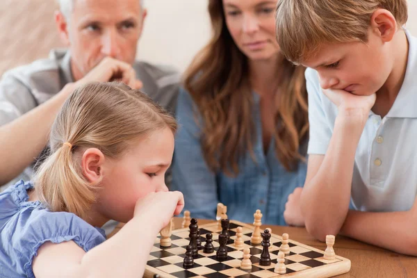 Niños enfocados jugando ajedrez frente a sus padres — Foto de Stock
