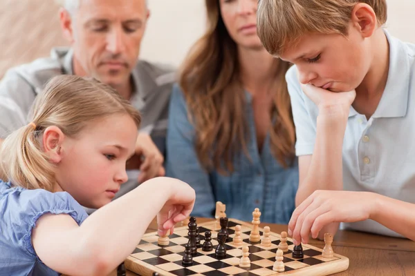 Сосредоточенные братья и сестры играют в шахматы на глазах у родителей — стоковое фото