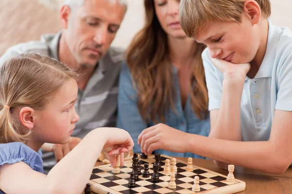 Primo piano dei fratelli che giocano a scacchi davanti ai loro genitori — Foto Stock