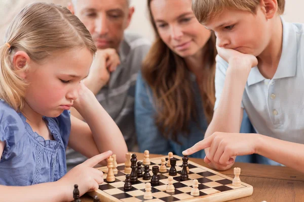 Primo piano dei bambini che giocano a scacchi davanti ai loro genitori — Foto Stock