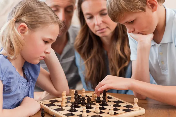 Close up of serious children playing chess in front of their par — Stock Photo, Image