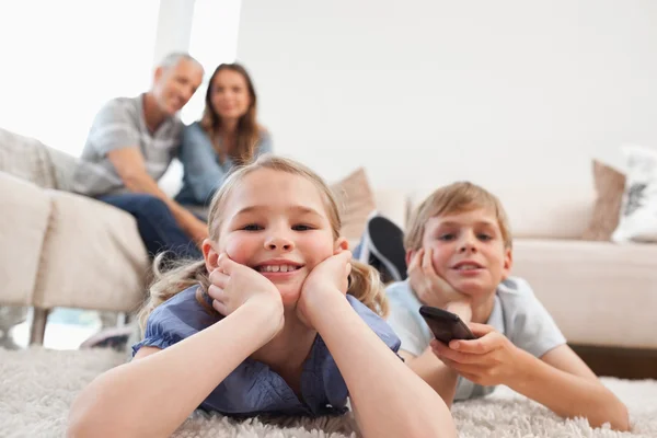 Братья и сёстры смотрят телевизор со своими родителями на заднем плане — стоковое фото
