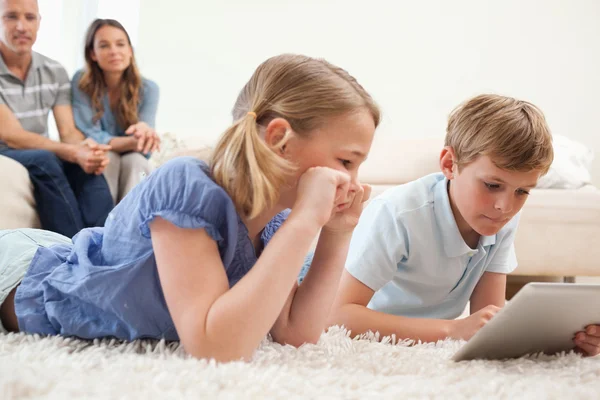 Niños usando una tableta con sus padres en la espalda — Foto de Stock