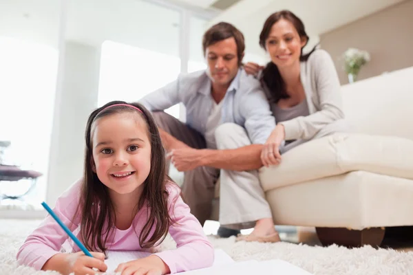 Girl drawing with her parents in the background — Stock Photo, Image