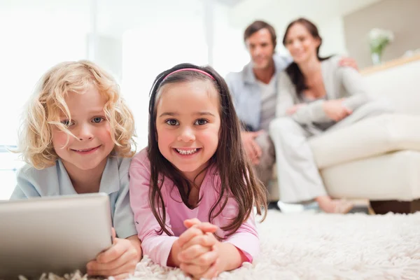 Siblings using a tablet computer while their parents are in the — Stock Photo, Image