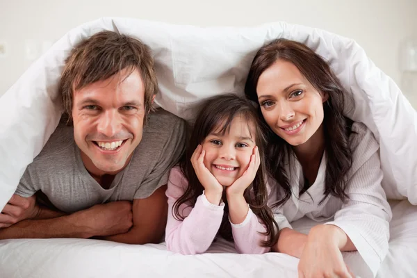 Батьки лежать під ковдрою зі своєю дочкою — стокове фото