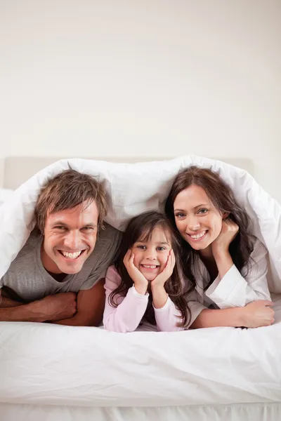 Retrato de padres acostados bajo un edredón con su hija —  Fotos de Stock