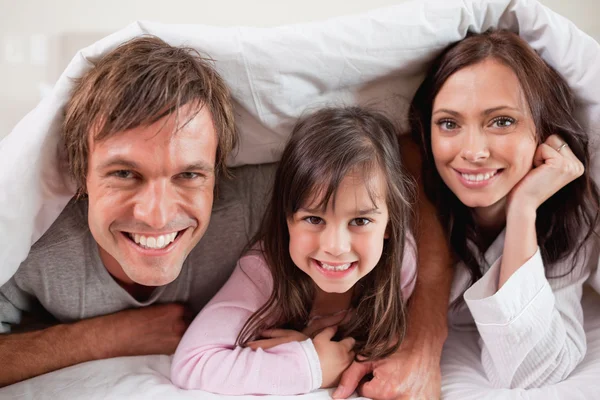 Šťastní rodiče ležící pod deku s jejich dcerou — Stock fotografie
