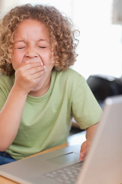 Porträtt av en pojke som gäspar medan du använder en bärbar dator — Stockfoto