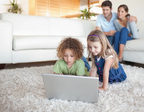 Children using a notebook while their parents are watching — Stock Photo, Image