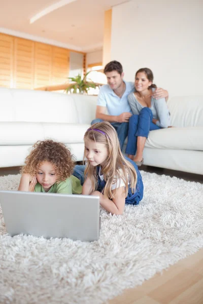 Portret van kinderen die gebruik maken van een laptop, terwijl hun ouders wa zijn — Stockfoto