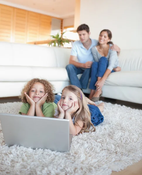Portrait of cute children using a notebook while their parents a — Stock Photo, Image
